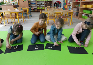 Dzieci układające fasolki na czarnych kartonach.